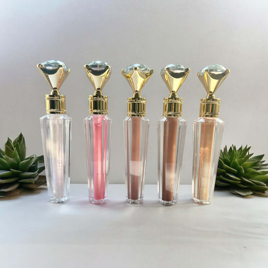 Cosmic Glam Infusion eco-friendly shimmer lip gloss collection with gold and crystal caps in various shades displayed with succulents