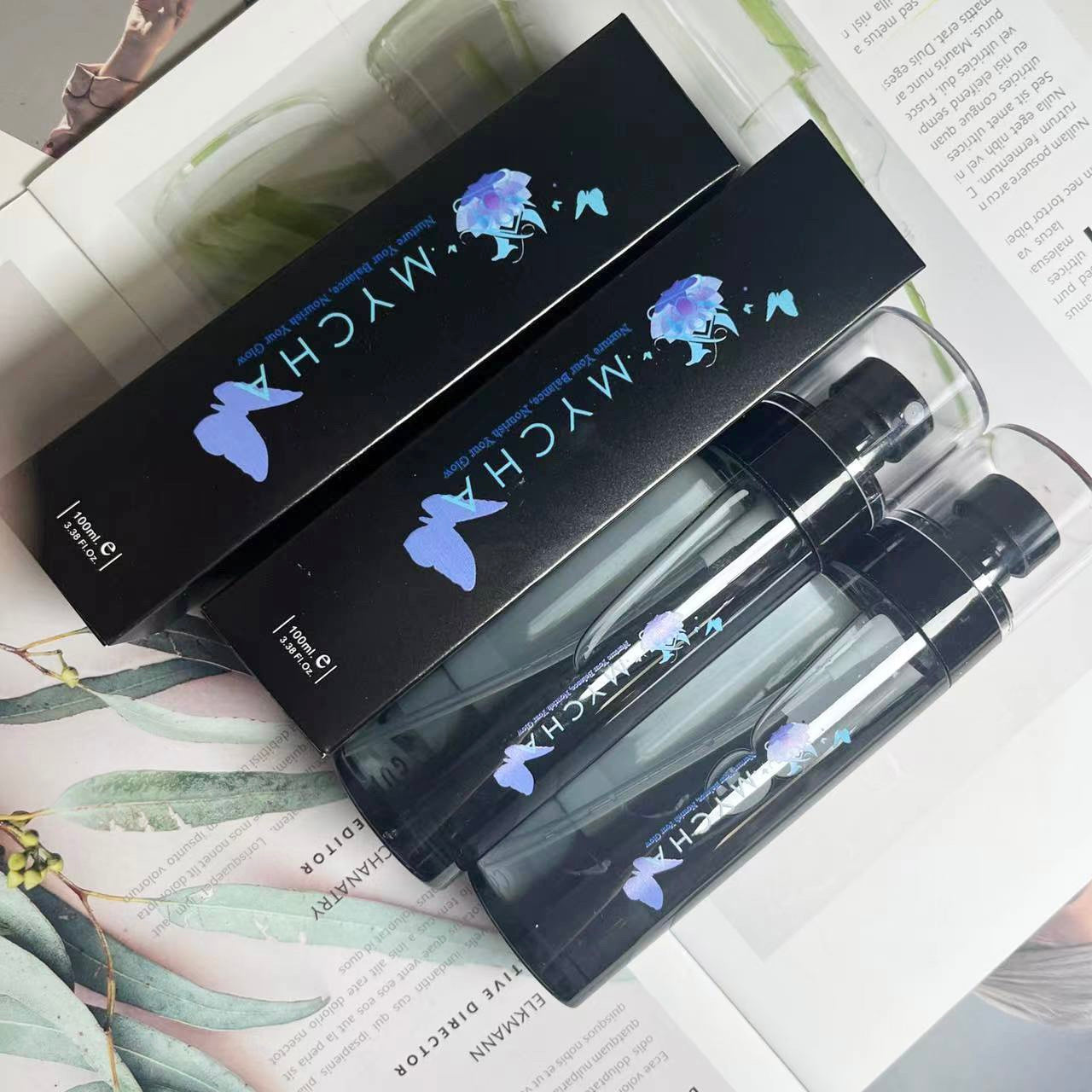 Arctic Glow Setting Mist packaging and bottle with black sleek design and blue floral logo on open magazine background