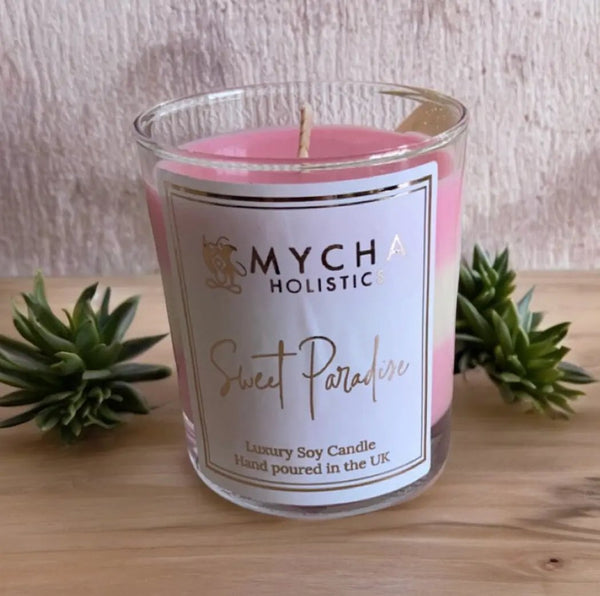 Sweet Paradise luxury soy candle by Mycha Holistics with pink wax, handmade and vegan, placed on wooden surface with green succulents.