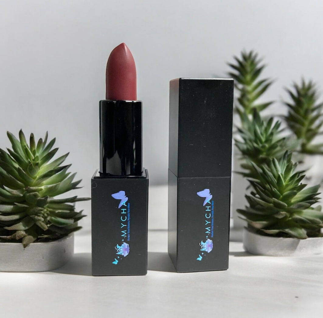 Silk Touch Matte Lipstick in sleek black packaging with a deep rose shade, displayed with green succulent plants background
