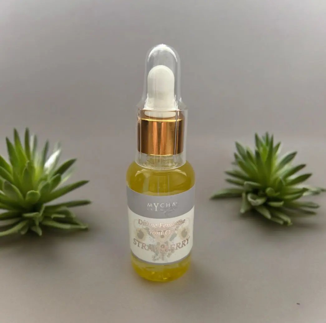 Bottle of Divine Feminine Yoni Oil with strawberry scent and dropper cap surrounded by green succulents