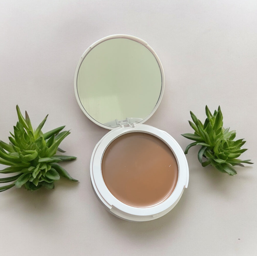 GlowUp CC Cream compact with mirror open showing creamy foundation surrounded by green succulents