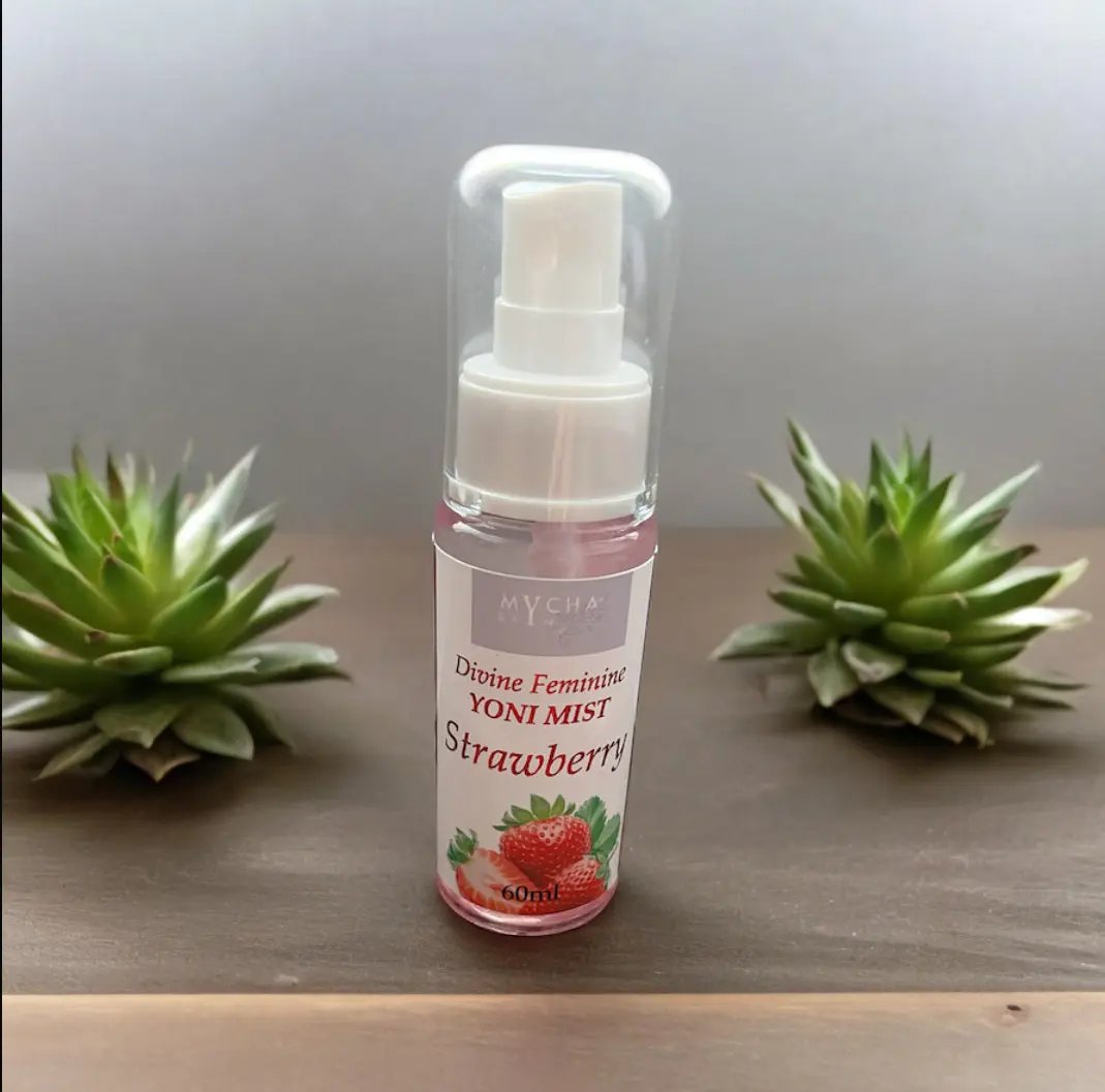 Divine Feminine Yoni Mist strawberry scent 60ml bottle with spray nozzle and green succulent plants on wooden surface