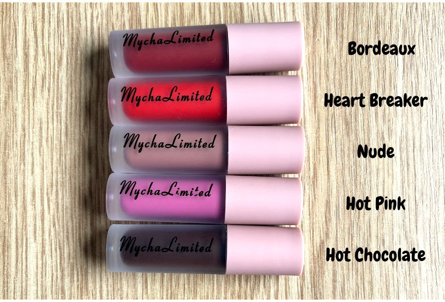 Opulent Matte liquid lipsticks in shades Bordeaux, Heart Breaker, Nude, Hot Pink, and Hot Chocolate with pink caps on wooden surface