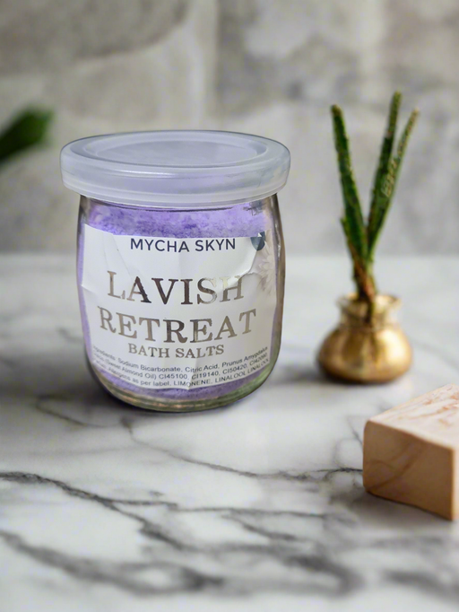 Lavish Retreat Foaming Bath Salts in a glass jar on marble surface with decorative plant in background